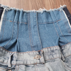 Detail of high waist denim jeans with patchwork design, frayed edges and metal button