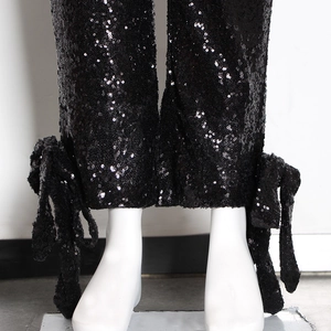 Dettaglio dei pantaloni con paillettes nere che mostra il tessuto lucido e il fiocco alla caviglia