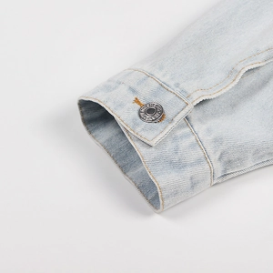 Detailed macro view of light blue denim cuff with silver metal button and fine stitching