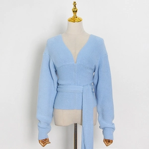 Detail of light blue V-neck knitwear featuring a waist tie and ribbed cuffs on a white backdrop
