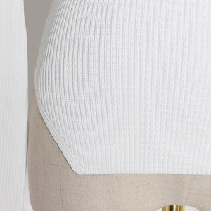 Detailed close-up of white ribbed knit fabric texture with irregular side slit hem design