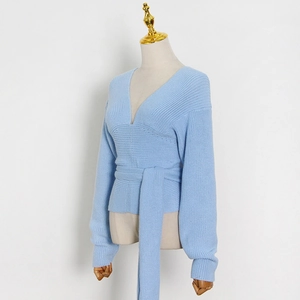 Detail of light blue knit sweater with V-neck, waist tie, and ribbed texture