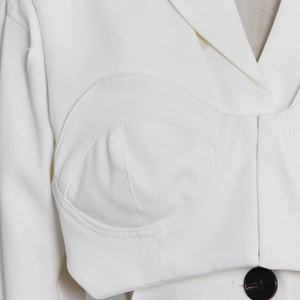 Close-up of white cropped blazer bustier top with padded shoulders and black button