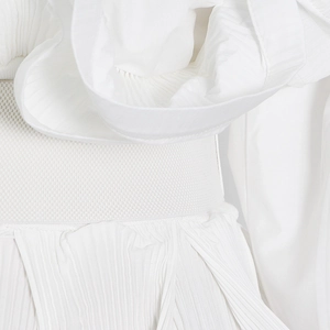Detailed macro view of white pleated fabric and elastic ribbed waist on long sleeve blouse