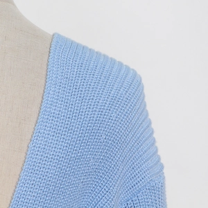 Detail view of light blue knitwear showing the soft fabric texture and V-neckline shoulder seam