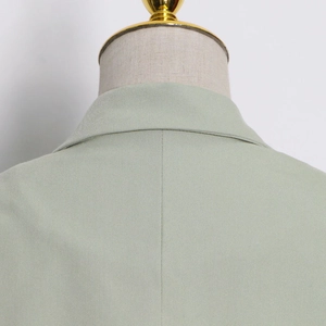 Detail of the stitching and twill texture on the shoulder of a sage green trench coat