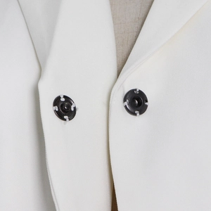Detail shot of black metal snap buttons on a white textured blazer with precise stitching