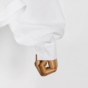 Detail of white shirt sleeve featuring pleated cuffs and single button closure on a hand model