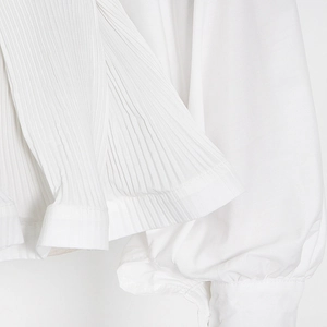 Detailed close-up of white shirt featuring intricate pleated cuffs and soft chiffon fabric