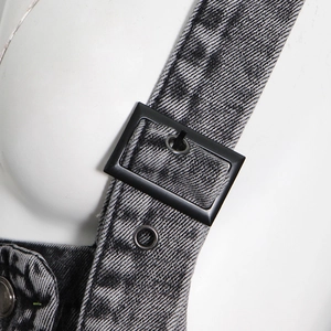Détail macro de la boucle métallique noire réglable et des œillets sur denim délavé