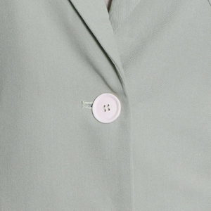 Detail of light green twill fabric trench coat with white button and V-neckline