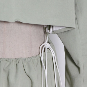 Detail of light green trench coat featuring elastic waist design and white drawstring