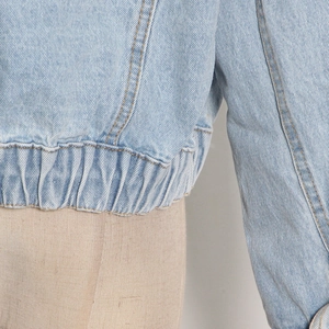 Dettaglio di una giacca in denim azzurro con orlo elastico e trama di cucitura precisa