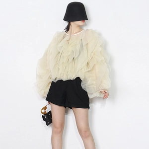 Detail of ruffle layers on a sheer beige French style blouse with chic crew neck