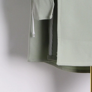 Detail of light green trench coat featuring side slit design and precise double-needle stitching