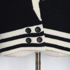 Détail du cardigan noir montrant l'ourlet côtelé à rayures blanches et les boutons noirs