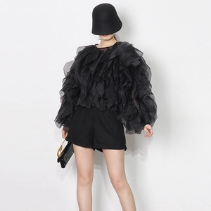 Detail of black tiered organza ruffle blouse paired with minimalist shorts and hat