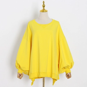 Detail of loose yellow sweatshirt featuring ribbed cuffs and side slit hem design