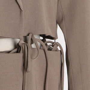Close-up of waist cutout detail with intricate tie-up strings on a cropped brown blazer