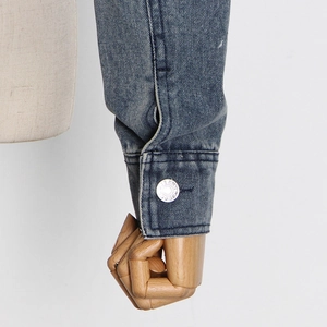 Detail of denim sleeve cuff with silver metal button and textured blue wash fabric