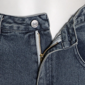 Detailed close-up of dark blue washed denim waist with metal zipper and jeans button