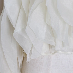Detail of white semi-transparent organza blouse showing delicate layered ruffle design
