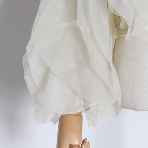 Macro shot of tiered ruffle sleeve detail on a white chiffon shirt with soft pearly sheen