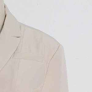 Detail of beige suit blazer showing structured shoulder pads and notched lapel