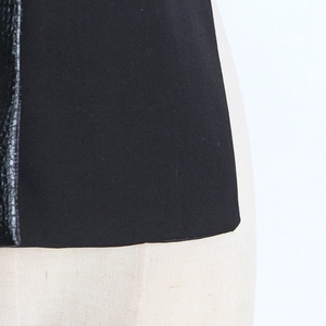 Détail du patchwork en cuir noir et tissu sergé mat sur un gilet cintré pour femmes