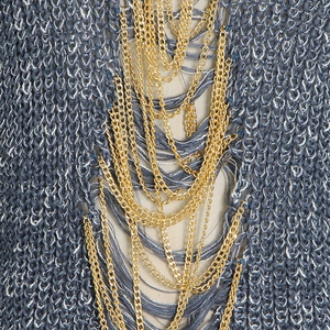 Close-up of heavy knit sweater with distressed cut-outs and layered gold chain detail