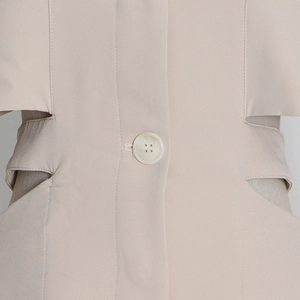 Detail view of the beige blazer featuring unique waist cut-outs and a yellow resin button