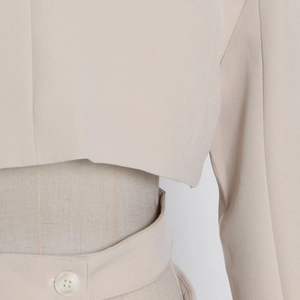 Detail of beige cropped blazer showing smooth fabric texture and button on the hemline