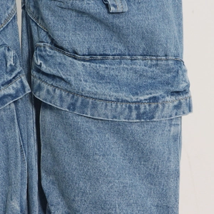 Detail of washed grey cargo pants showing side flap pocket and yellow contrast stitching