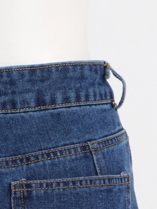 Detalle de la cintura alta de unos vaqueros con tela azul oscuro y costuras naranjas