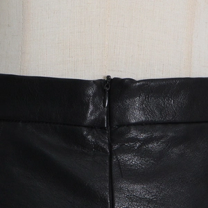 Detailed close-up of high-waisted black leather skirt with invisible side zipper