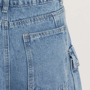 Detail view of denim cargo pants showing reinforced stitching and functional side flap pockets