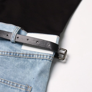 Detalle de cintura denim azul claro con etiquetas blancas y cinturón negro de piel