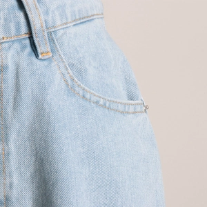 Dettaglio dei jeans a vita alta blu chiaro con cuciture arancioni e rivetti in metallo