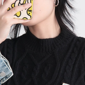 Detail of black cable-knit sweater paired with a light wash denim jacket and silver earrings
