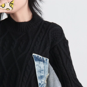 Detail of cable knit black sweater with frayed denim patchwork on the side and ribbed collar