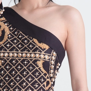 Détail d'une robe à épaule dénudée avec broderies de perles et motifs imprimés dorés