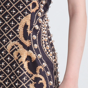 Détail d'une robe trapèze avec imprimé chaîne dorée et broderie de perles sur la couture
