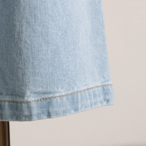 Dettaglio delle cuciture arancioni a contrasto e texture denim azzurro sull'orlo
