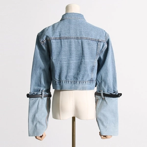 Detail view of light blue denim jacket sleeve with black strap buckle decoration