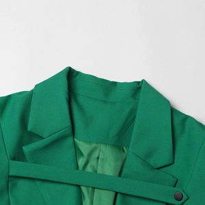 Détail macro du blazer vert émeraude avec revers cranté, lanière déco et bouton noir