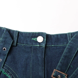 Detail of blue denim skirt waist with green stitching and metallic buckle accents