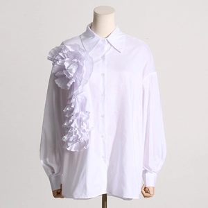 Dettaglio del grande fiore plissettato 3D su una camicia bianca a maniche lunghe