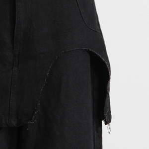 Dettaglio di pantaloni in denim nero a vita alta con patchwork asimmetrico e bordi grezzi