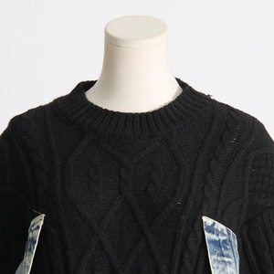 Detail of cable knit black sweater with blue denim patchwork and distressed texture