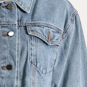 Close-up of light blue denim jacket with orange contrast stitching and metal buttons